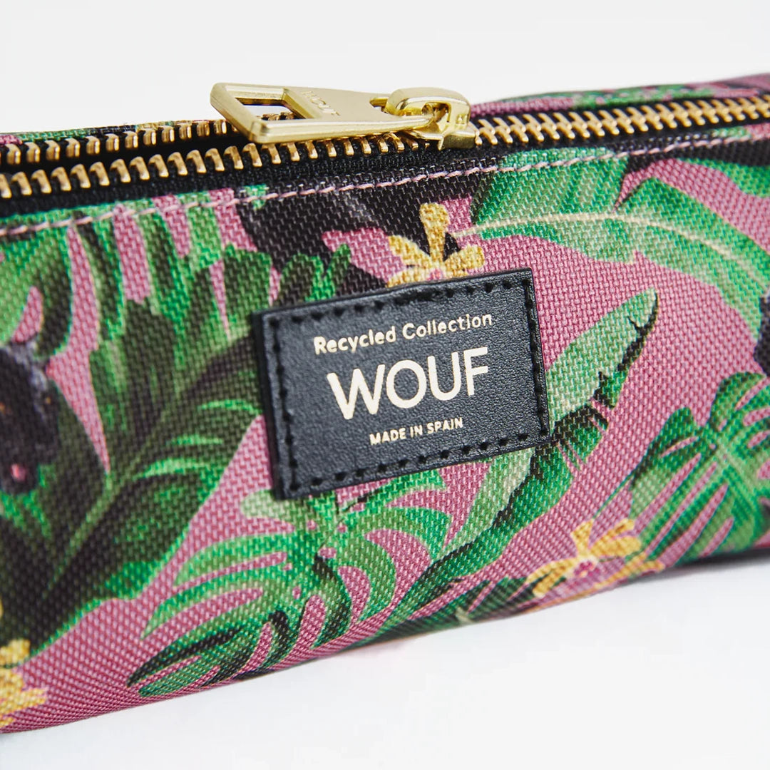 Vue rapprochée de la trousse WOUF montrant l'étiquette avec le logo et le texte "Recycled Collection" sur un fond d'imprimé tropical avec fermeture éclair dorée
